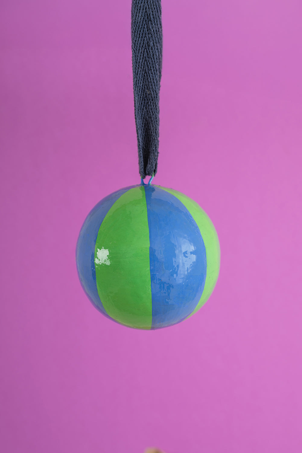 Two-toned green and blue christmas bauble decoration with a string on a pink background