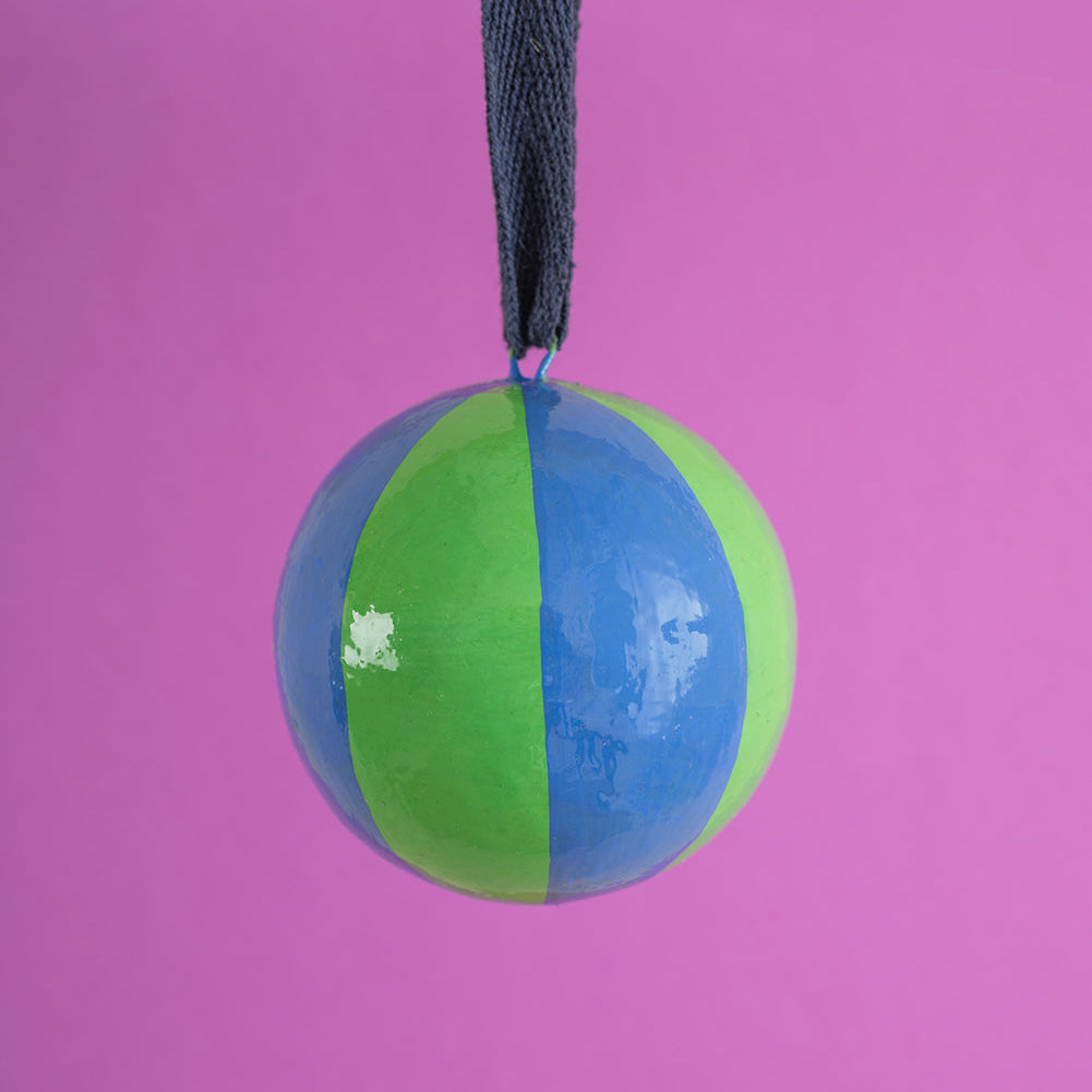 Two-toned green and blue christmas bauble decoration with a string on a pink background