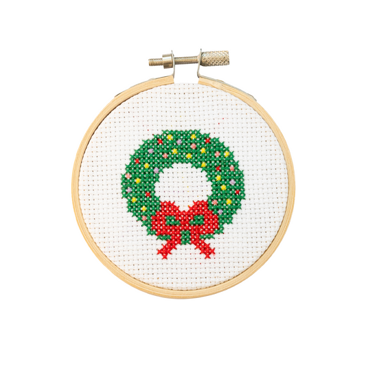 Cross-stitched Christmas wreath with a red bow in a wooden hoop on a white background