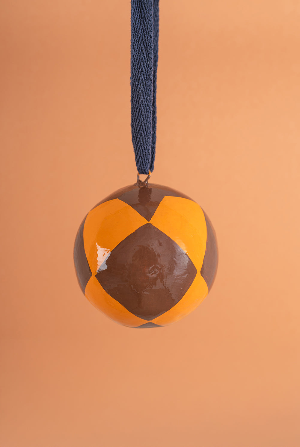 hand painted bauble with brown and orange pattern on a blue string against an orange background