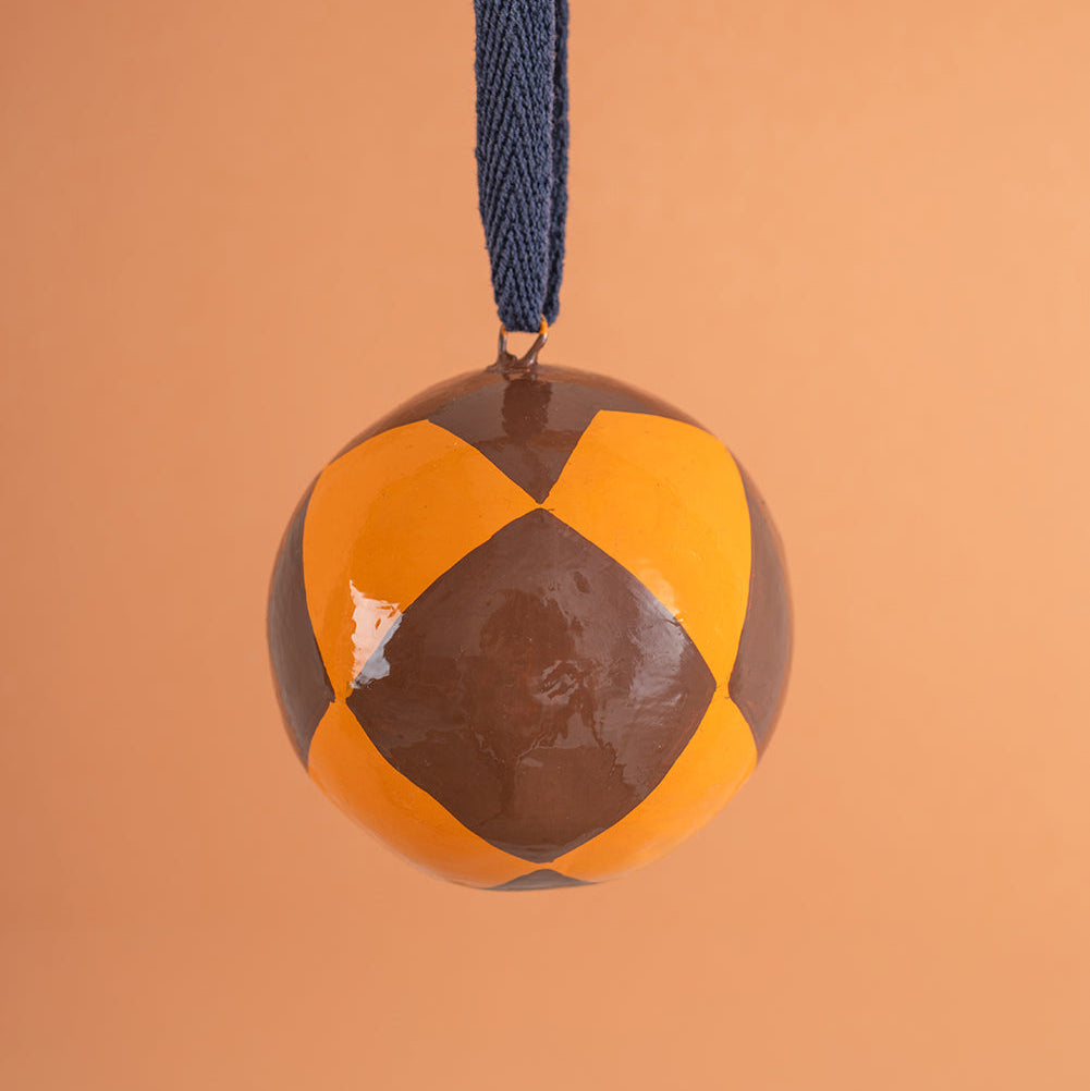 hand painted bauble with brown and orange pattern on a blue string against an orange background