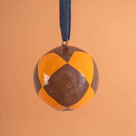 hand painted bauble with brown and orange pattern on a blue string against an orange background