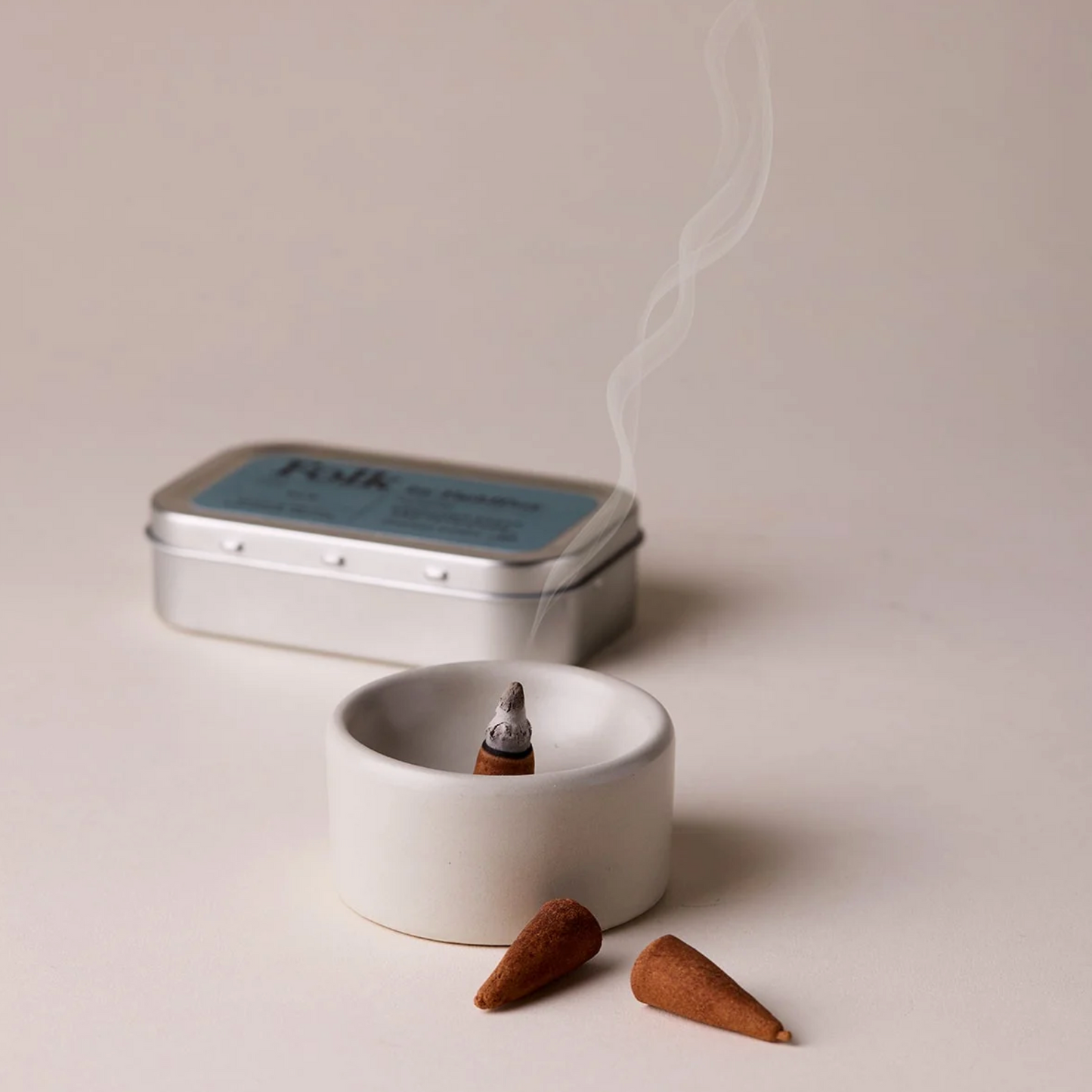 Incense cones and a small white dish with smoke on a light background
