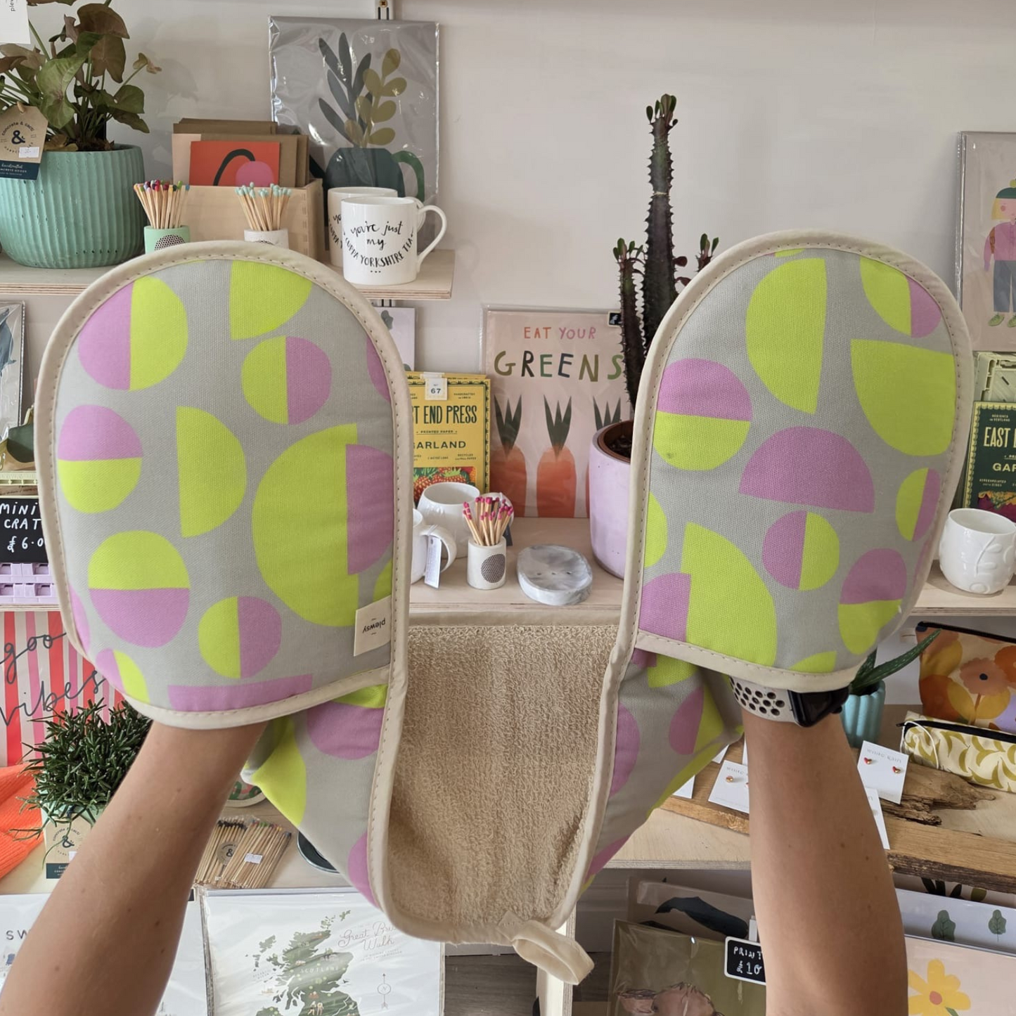 Pair of yellow and pink patterned slippers worn by a person in a room with shelves and plants.