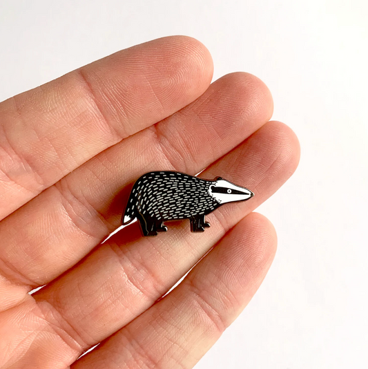 Badger-shaped pin held between fingers on a white background