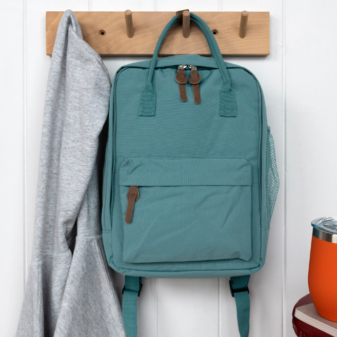 Blue backpack hanging on a wooden hook with a gray sweater and orange mug in the background.
