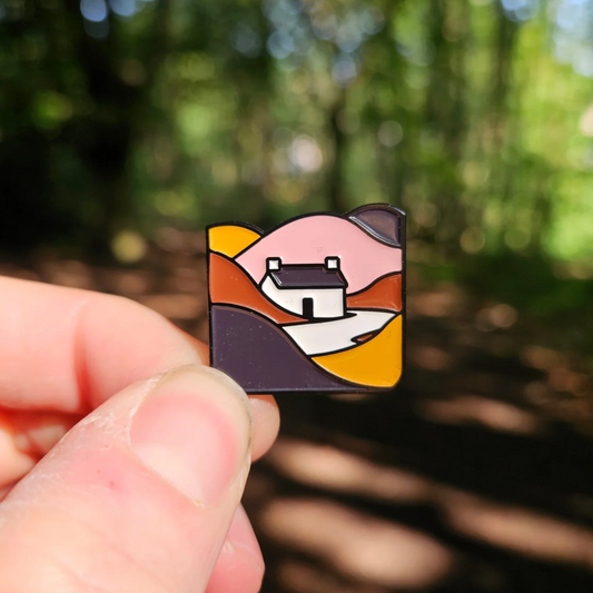 Pin with a landscape design on a pin badge held by a hand against a blurred natural background