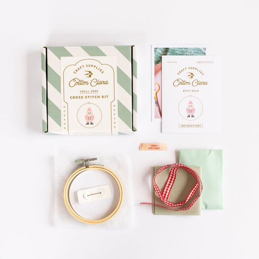 Cross-stitch kit with box, hoop, thread, and instructions on a white background