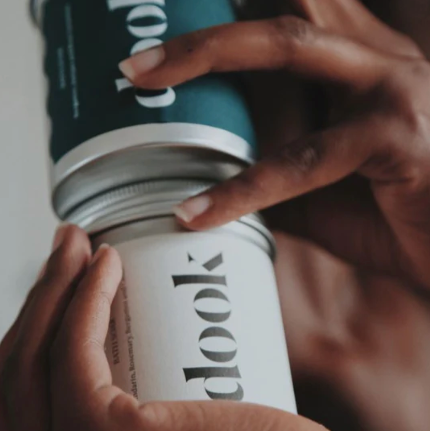 Two cans of 'Dook' product held by hands against a neutral background