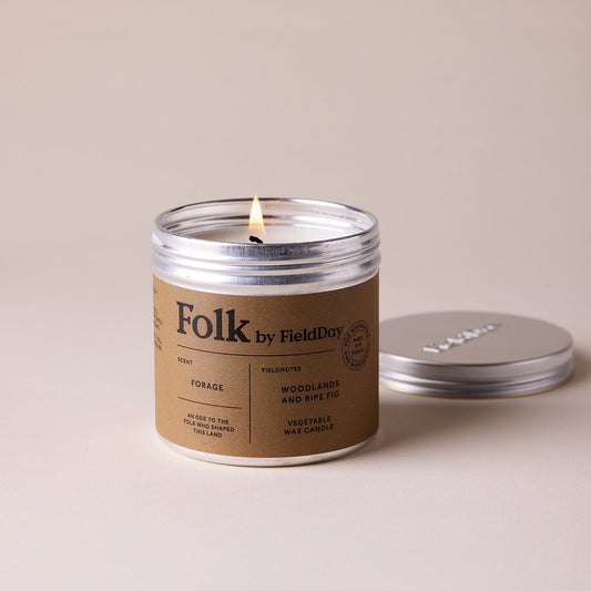 Candle in a 'Folk by Field Day' tin with a lit wick on a beige background