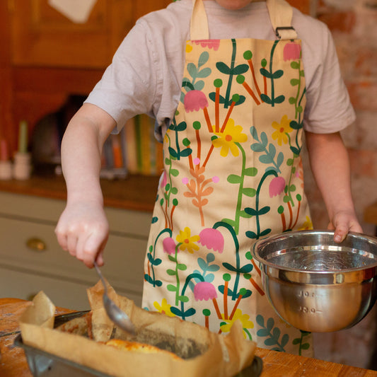 A child wearing a floral apron with a design of various flowers in multiple colors, helping with cooking.
