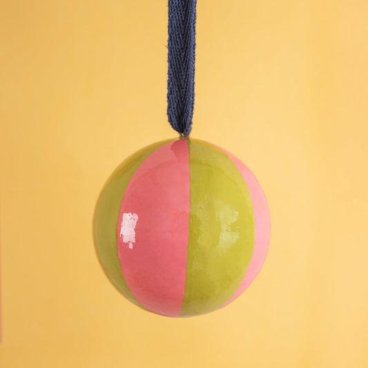 Two-toned pink and green christmas bauble with a blue rope on a yellow background