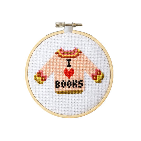 Cross-stitched design of a sweater with 'I love books' text in a wooden hoop on a white background