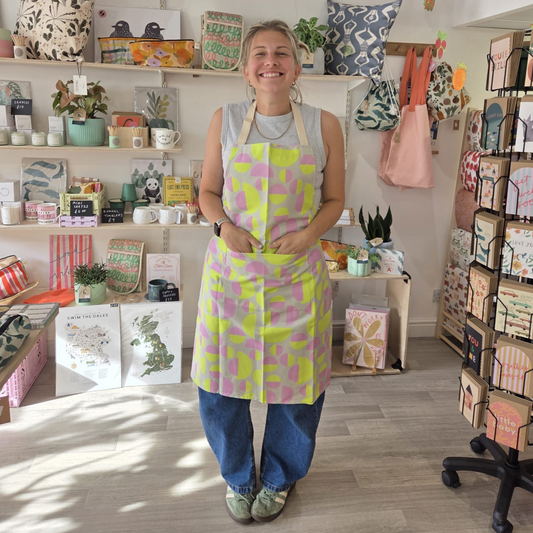 Person wearing a colorful apron in a store setting with shelves and products.