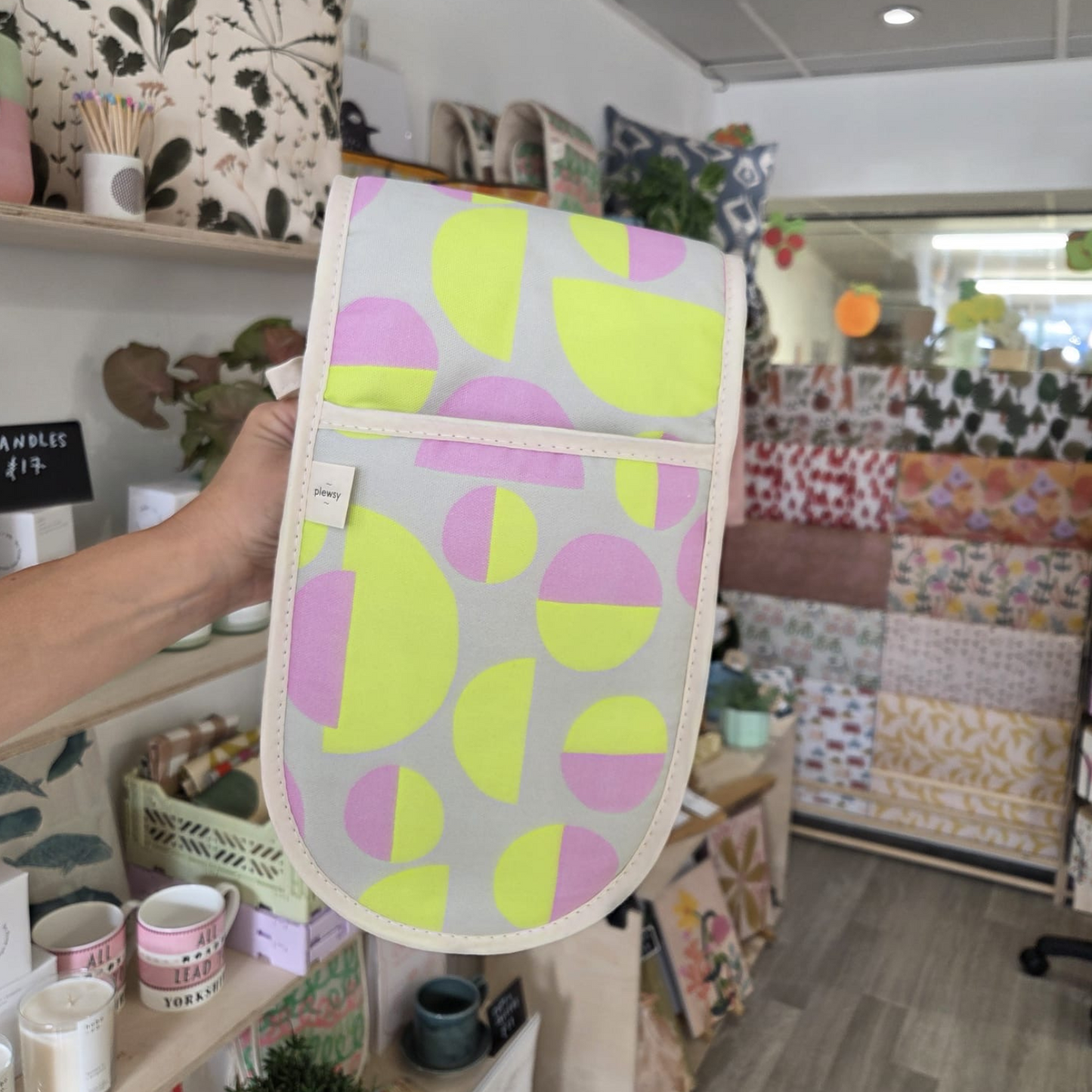 Person holding a patterned oven mitt in a store with fabric displays in the background