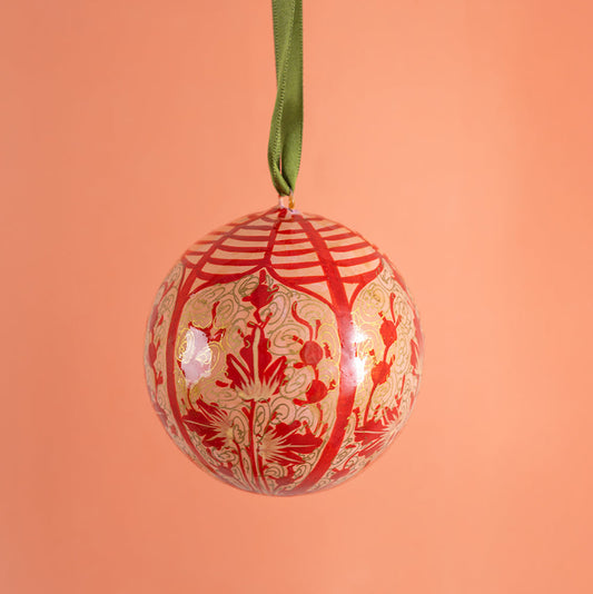 Decorative Christmas ball ornament with red and gold pattern on a peach background