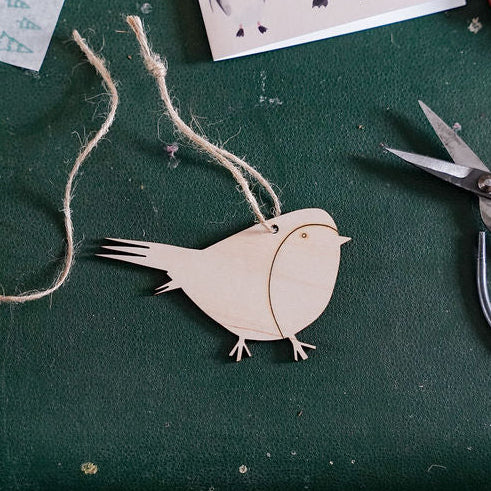 A wooden bird-shaped ornament with a twine loop, displayed on a dark green suitcase next to scissors, twine, and small decorative items.