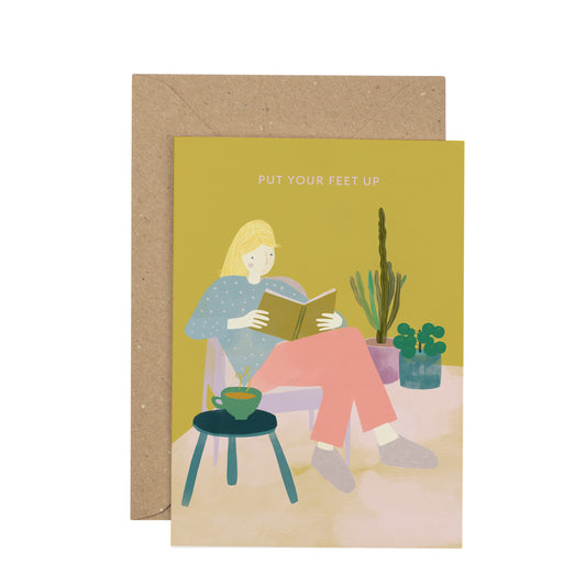 Greeting card with illustration of a person reading a book, sitting on a chair with plants around, and a brown envelope.