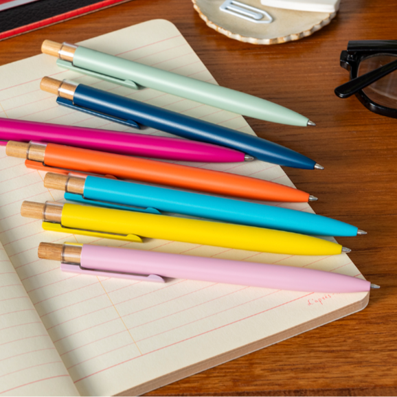 Colorful recycled aluminium ballpoint pens on a notebook with stationery items in the background.