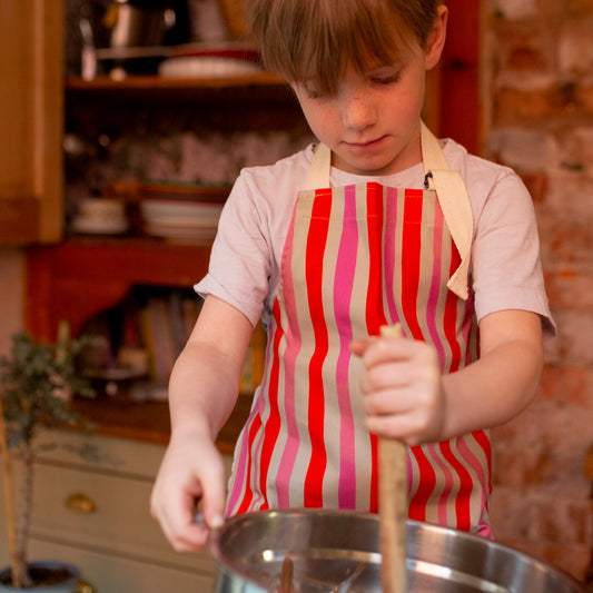 A child wearing a pink and red striped apron with adjustable strap