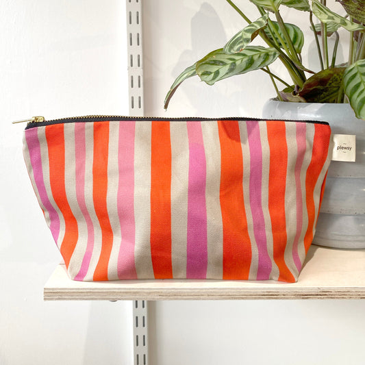 A striped cosmetic bag with red, pink, and orange vertical stripes, Printed on sustainable cotton, with a high quality YKK brass zip and natural panama cotton lining.