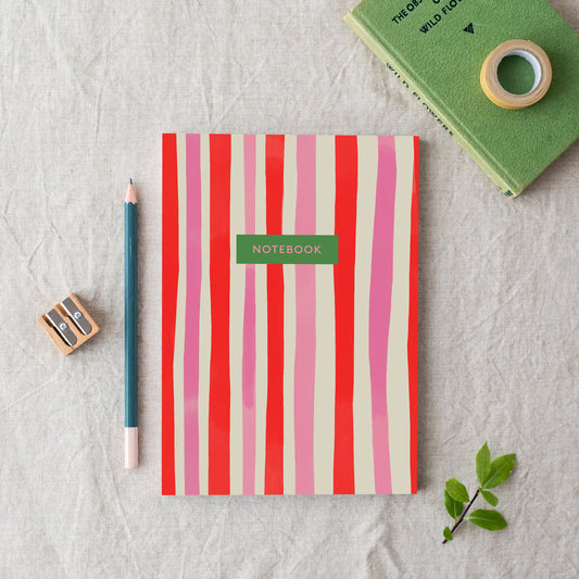 An A5 notebook with red and pink vertical stripes, labelled 'notebook', made in Britain from bleed proof, eco-friendly, recycled paper with 100gsm inner pages.