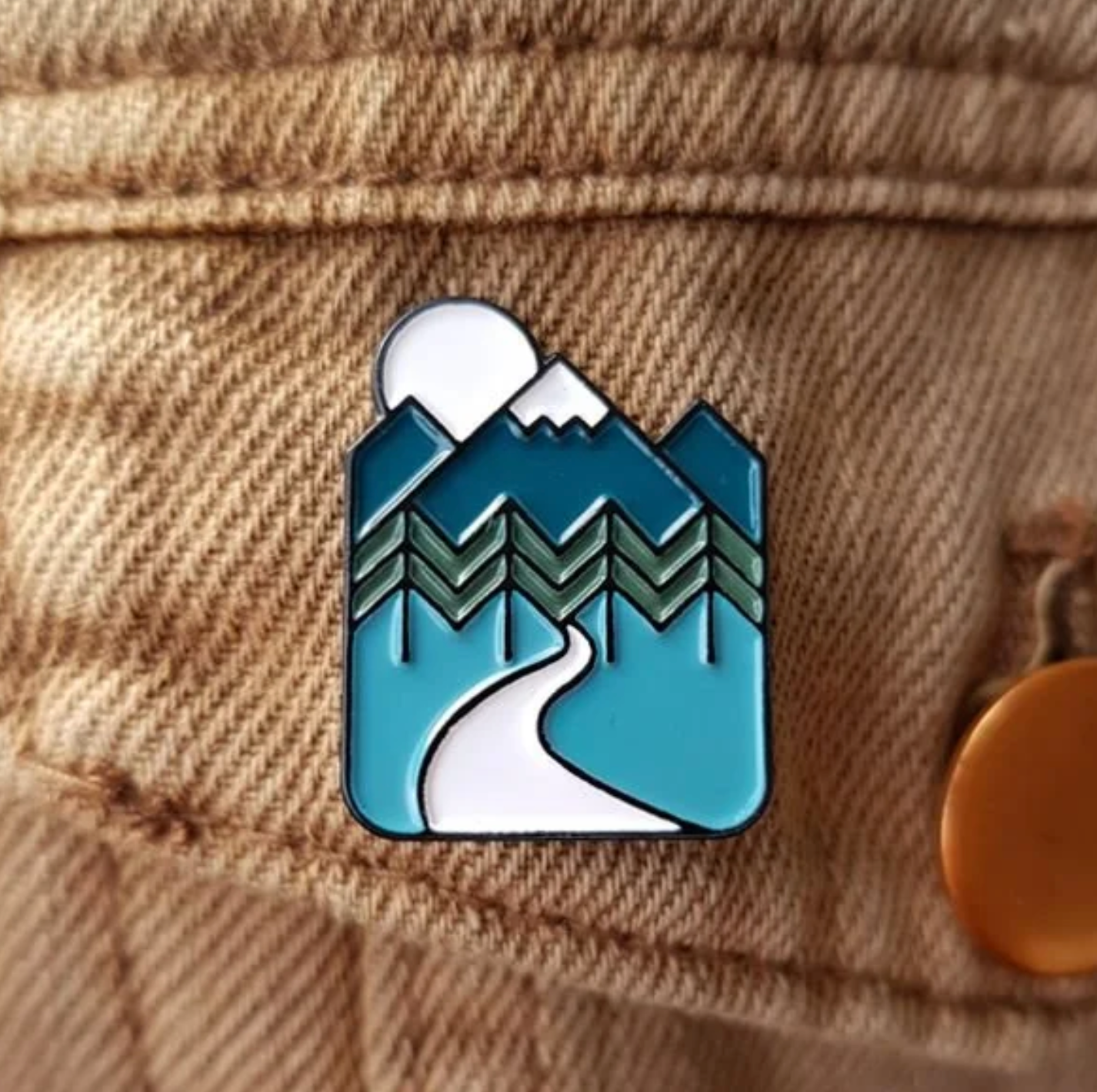 Pin with mountain and sun design on a denim jacket