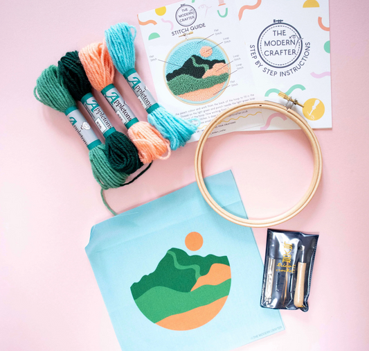 Embroidery hoop, threads, and stitch guide with mountain design on a pink background