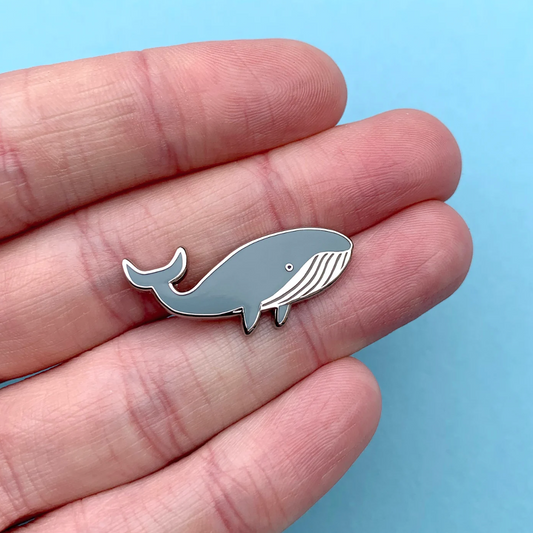 Small whale-shaped object held between fingers against a light blue background