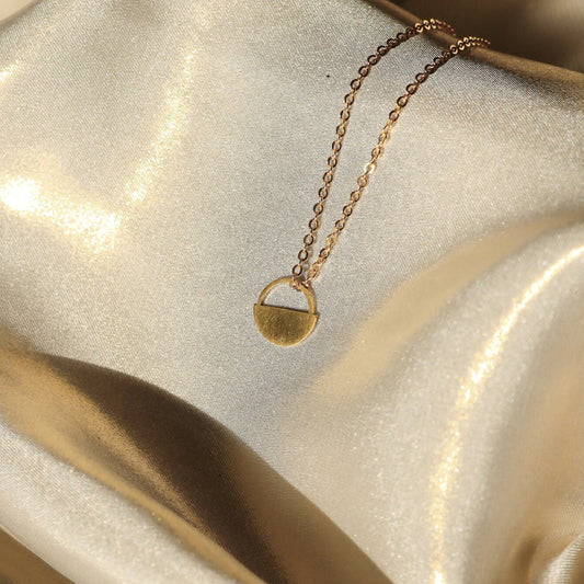 Gold necklace with a pendant on a textured beige surface