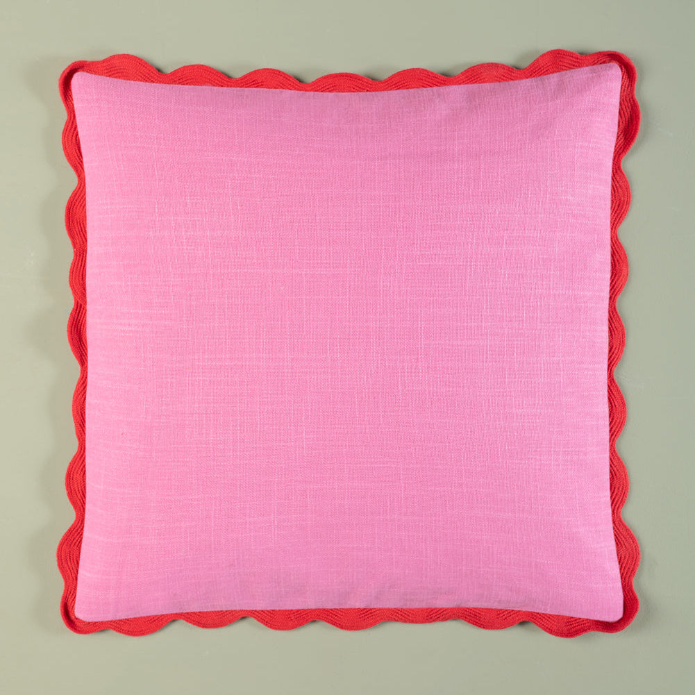 Pink pillow with red scalloped edge on a light gray background