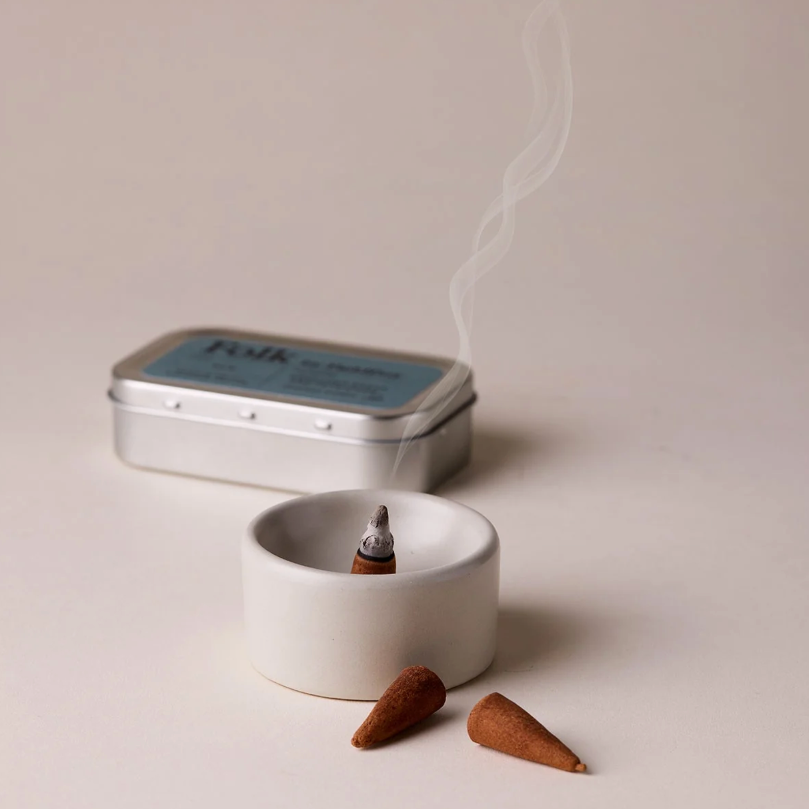 Incense cones and a small white dish with smoke on a light background