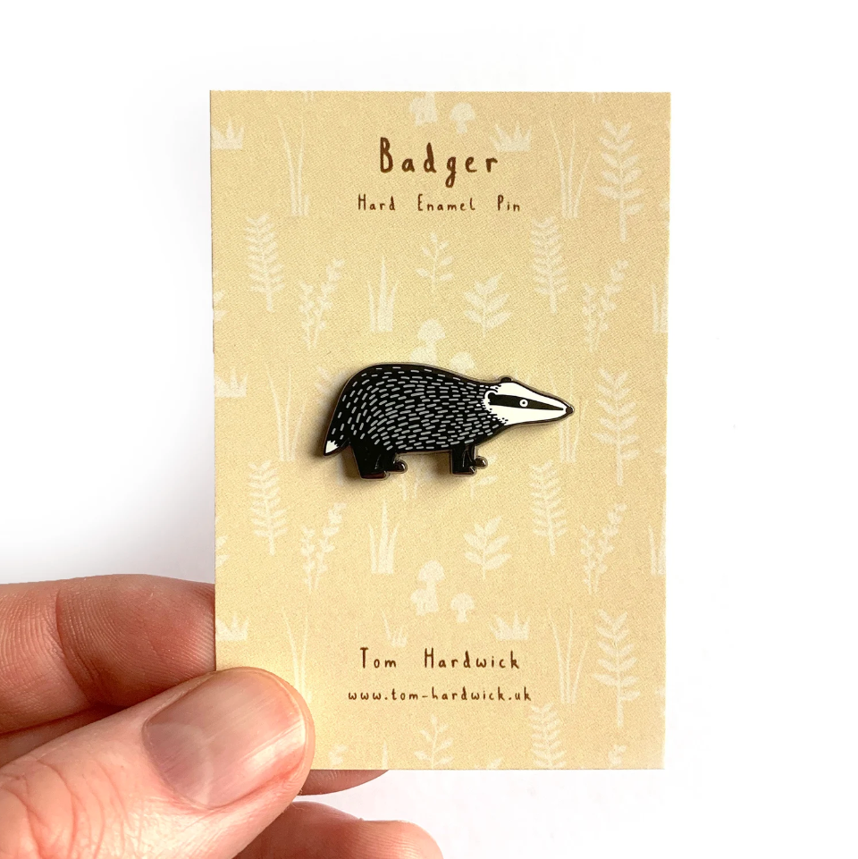 Badger enamel pin on a beige card held by a hand