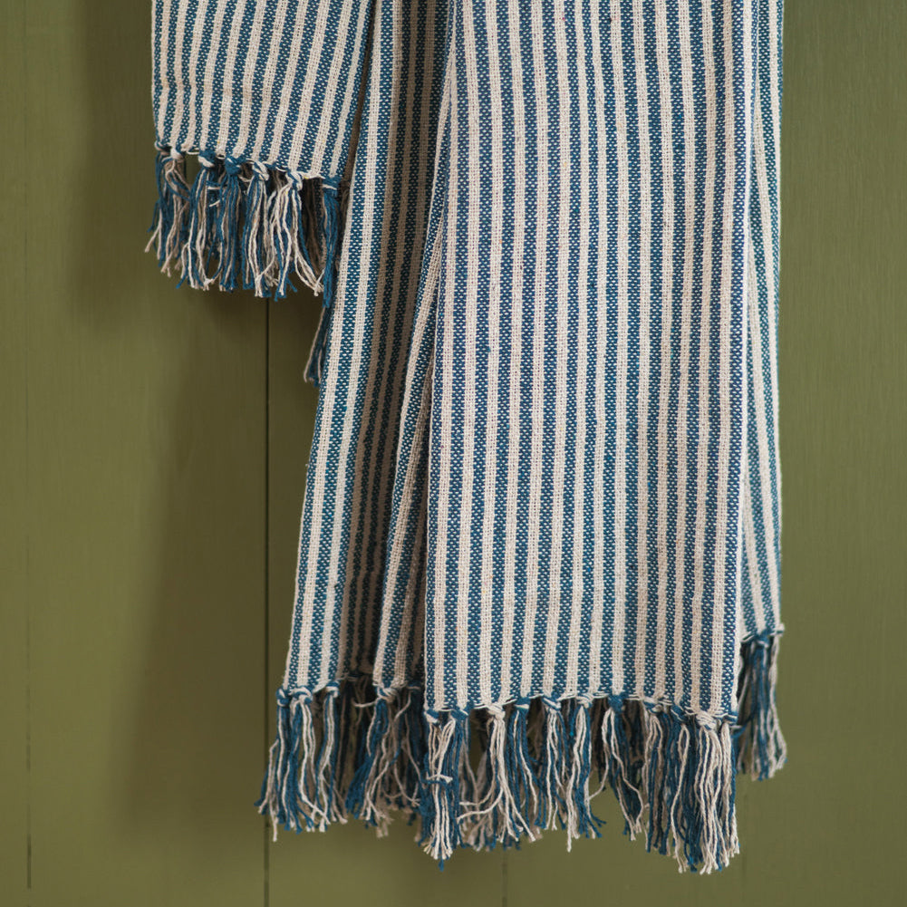 Blue and white striped 100% recycled cotton throw with fringes on a green background