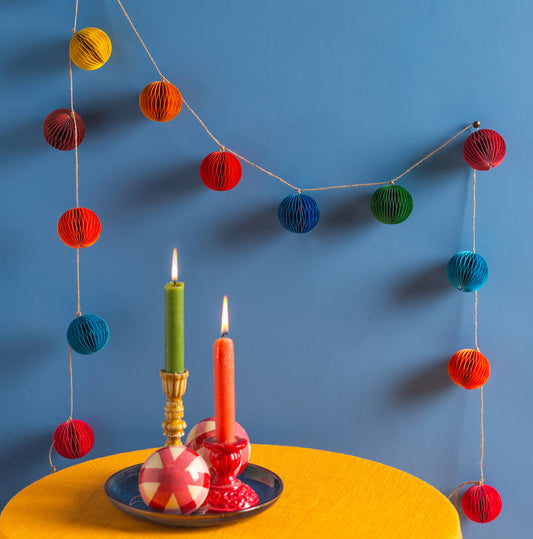 Decorative setup with colorful garland, candles, and apples on a yellow tablecloth against a blue background.