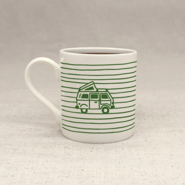 A white ceramic mug with a handle, decorated with thin green horizontal stripes and a green line-art illustration of a van with a tent on top, set against a neutral textured background.