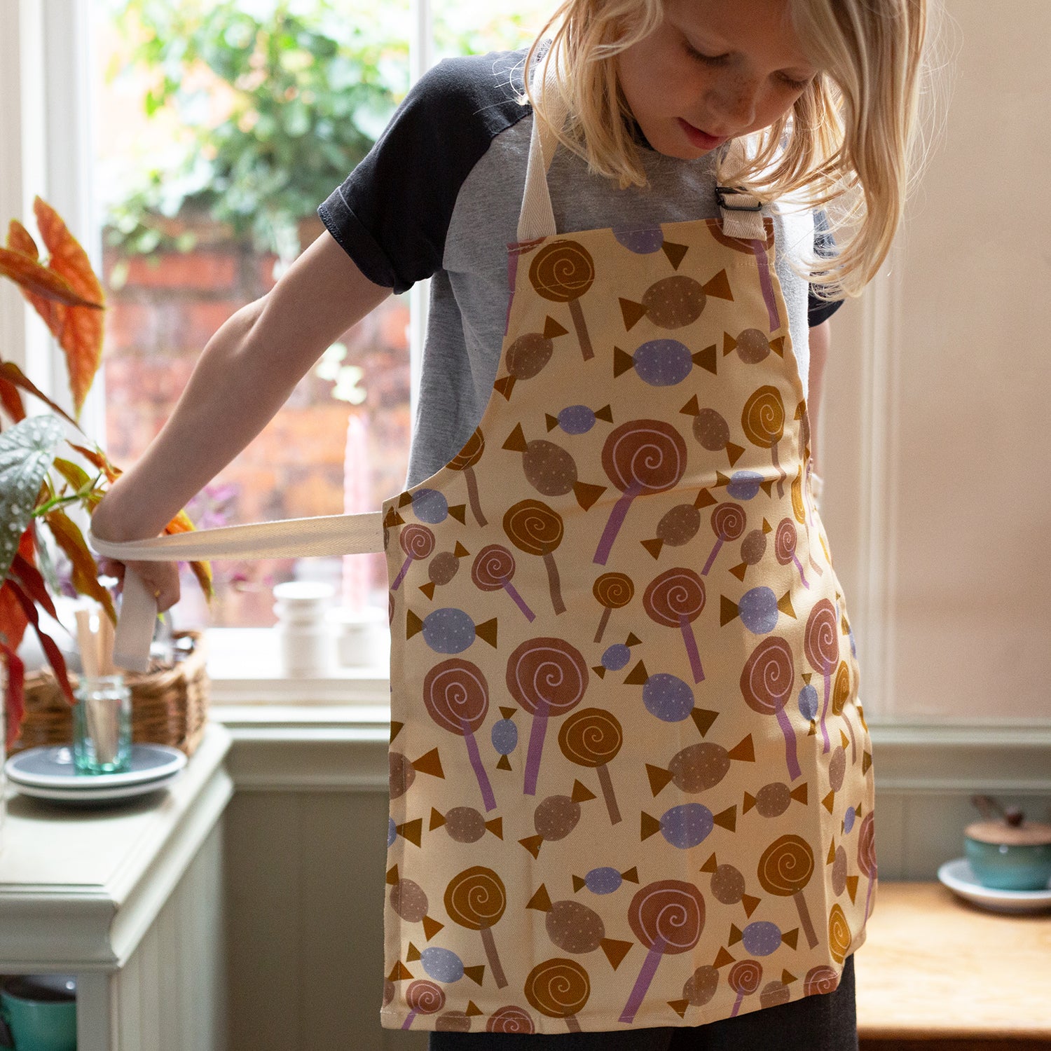 Child wearing a multicolored apron with candy patterns, adjustable neck strap.