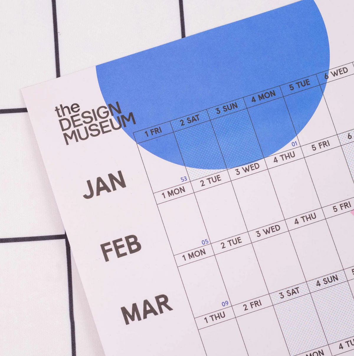A close-up of a monthly calendar page from The Design Museum, showing January, February, and March with a large blue abstract shape across the top on a white tiled background.