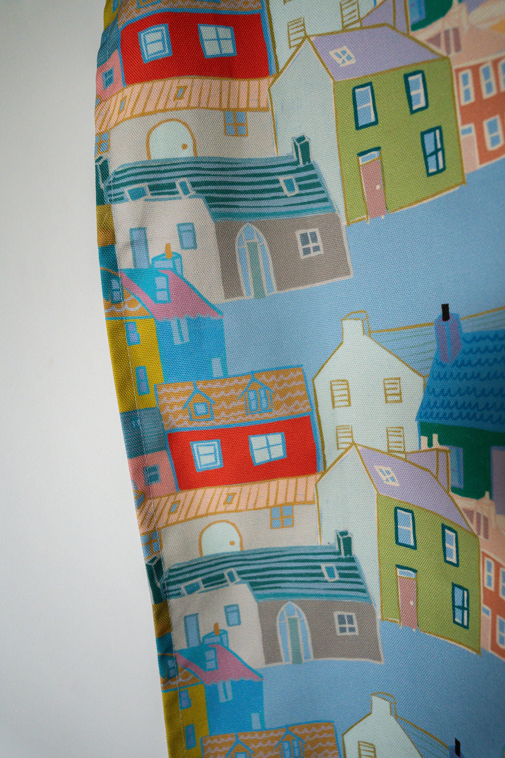 A close-up of a printed fabric featuring a whimsical, colourful illustration of houses with blue roofs and a light blue background.