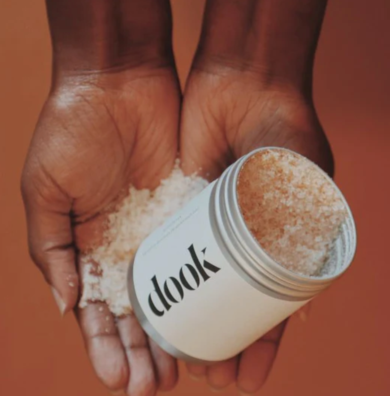 Person holding a container of 'dook' bath salts on a brown background