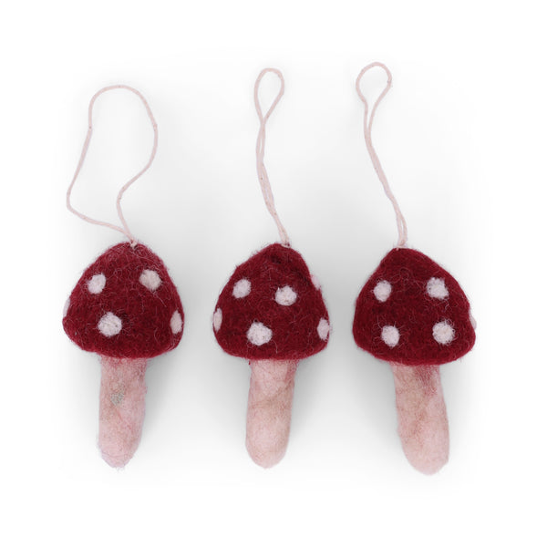 Three red mushroom-shaped felt ornaments with white spots on a white background