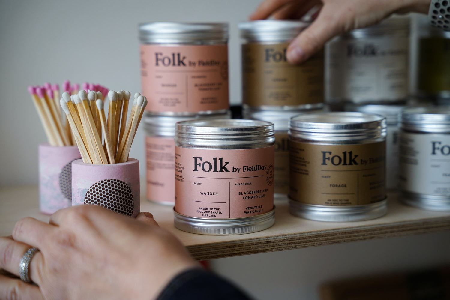 Folk by Field & Main candles on a shelf with hands interacting with them