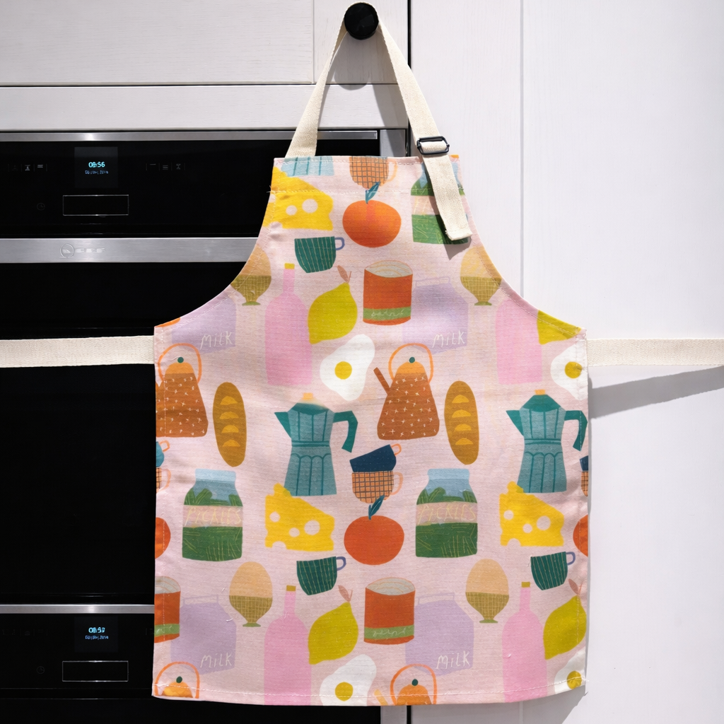 Colorful apron with food-themed design hanging on a white cabinet.