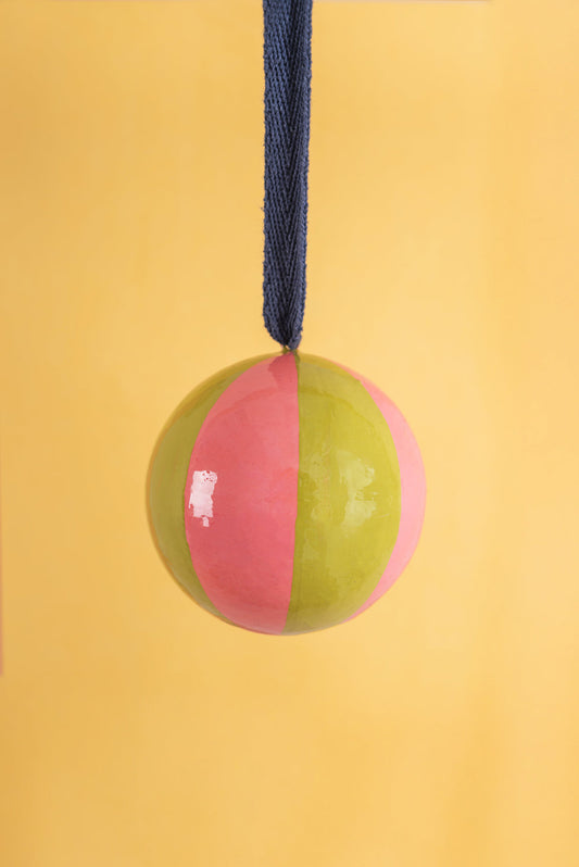 Two-toned pink and green christmas bauble with a blue rope on a yellow background