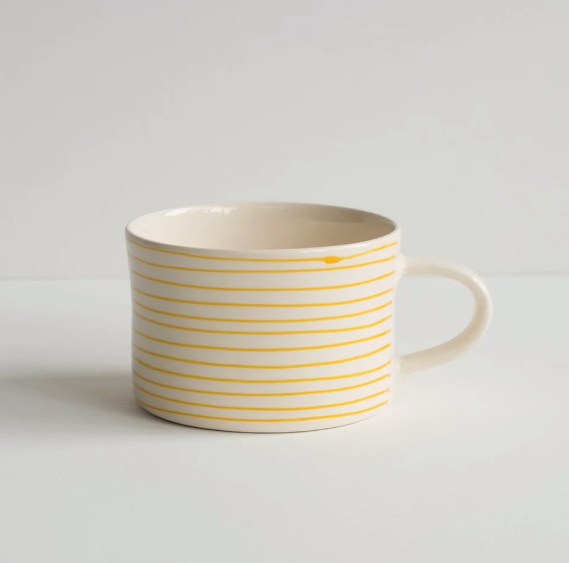 A white ceramic mug with thin yellow horizontal stripes, shown from a side angle against a plain white background.