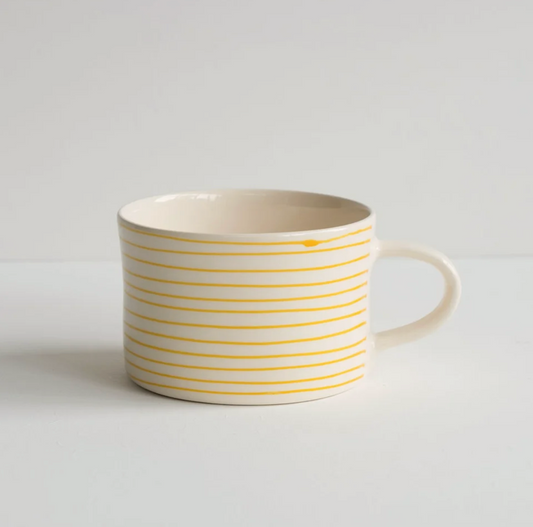 A white ceramic mug with thin yellow horizontal stripes, shown from a side angle against a plain white background.
