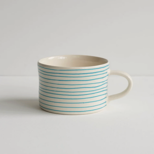 A ceramic mug with a cream-colored exterior and handle, decorated with thin, horizontal turquoise blue stripes, set against a plain light gray background.