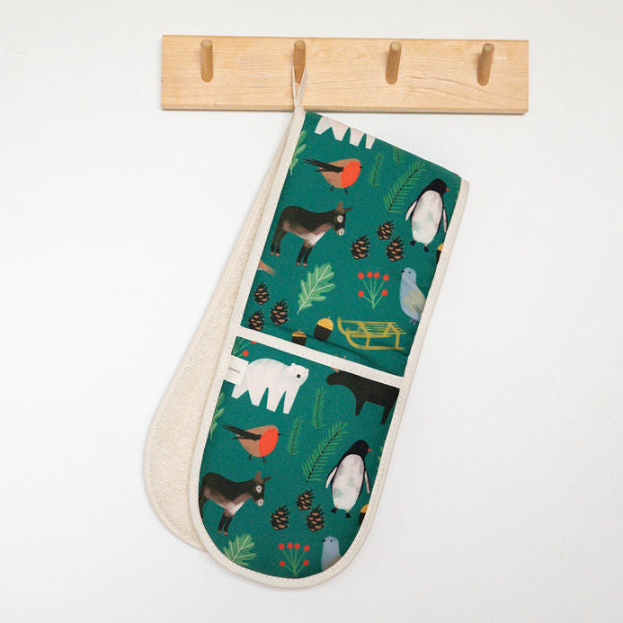 A fabric oven mitt with a green woodland bird pattern hangs from a light wood rack on a white wall, with a blue-gray wall cabinet visible above.