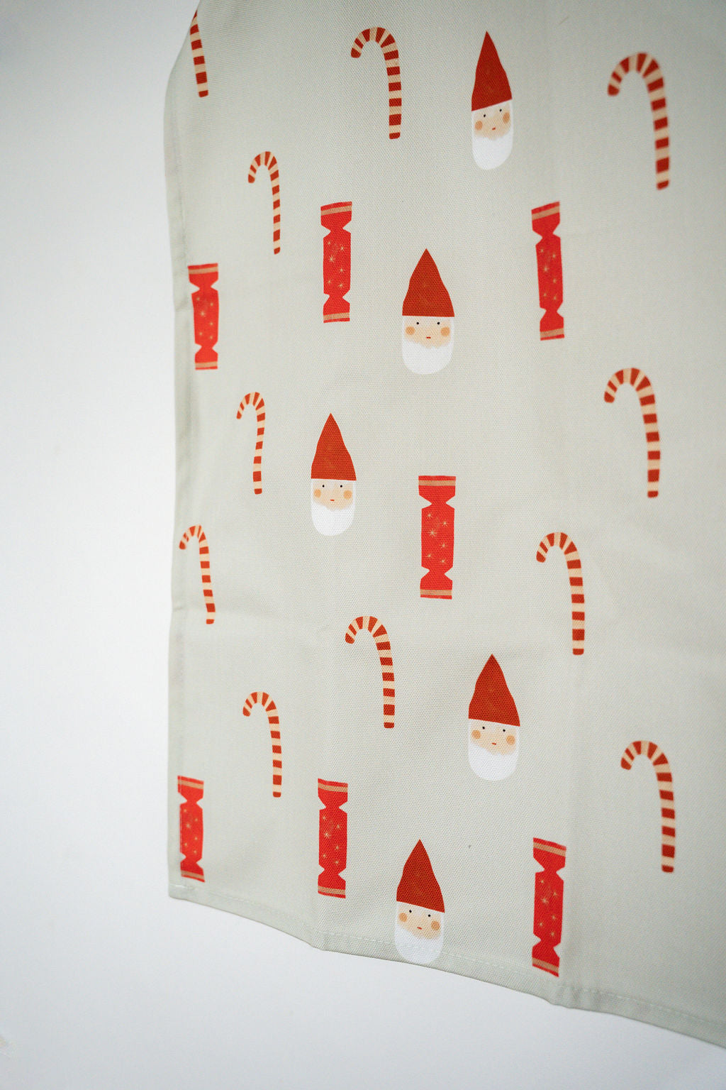 An off-white cotton tea towel featuring a festive Christmas pattern of red and white candy canes, Santa Claus faces, and red Christmas ornaments.