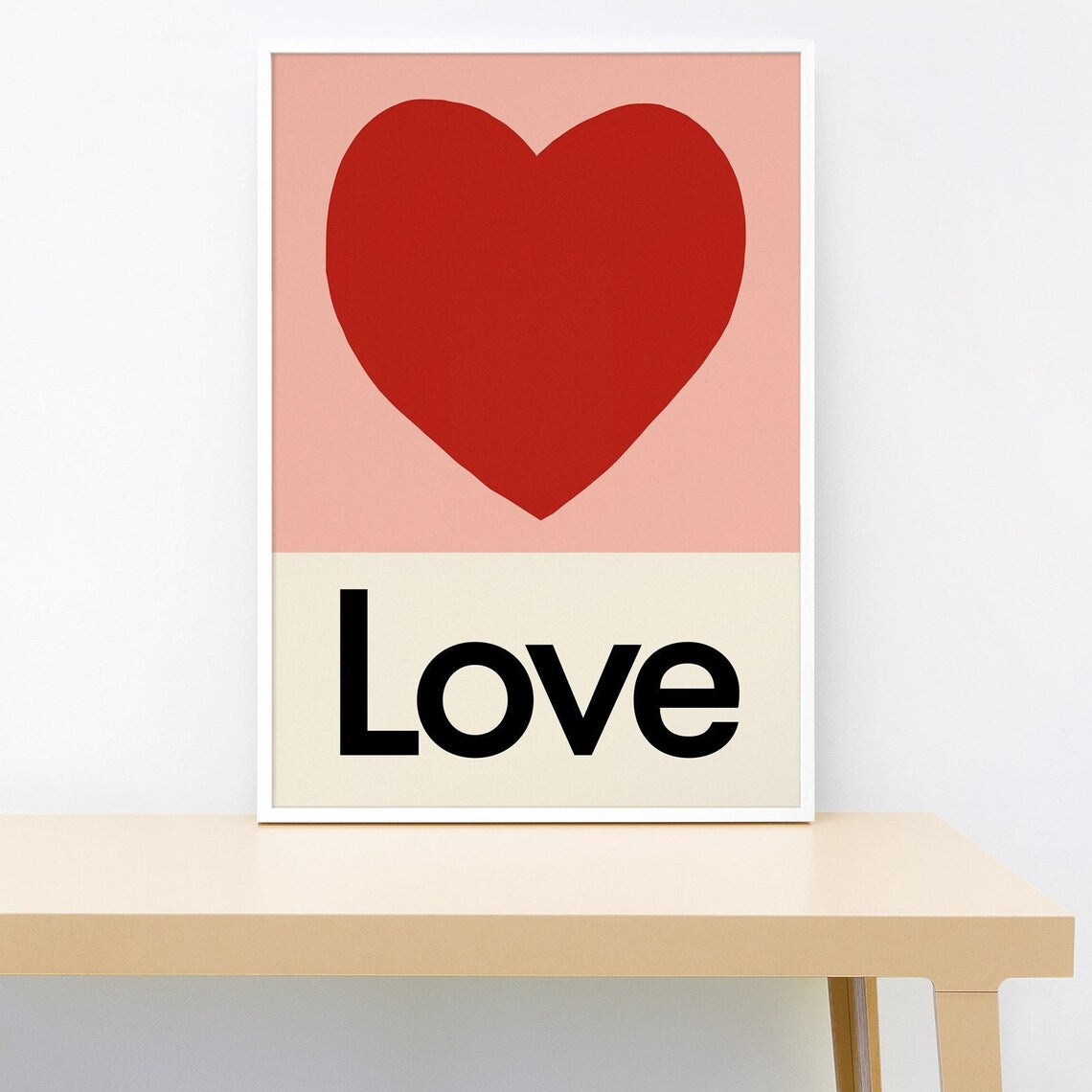 Poster with a red heart and the word 'Love' on a pink and beige background, placed on a wooden surface.